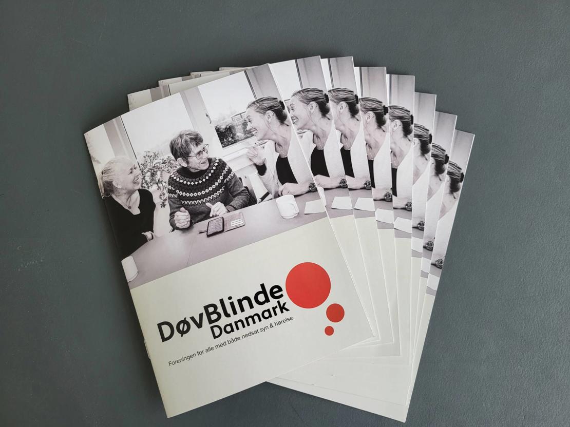 Pjecens forside med to døvblinde og en kontaktperson, der alle smiler og kommunikerer