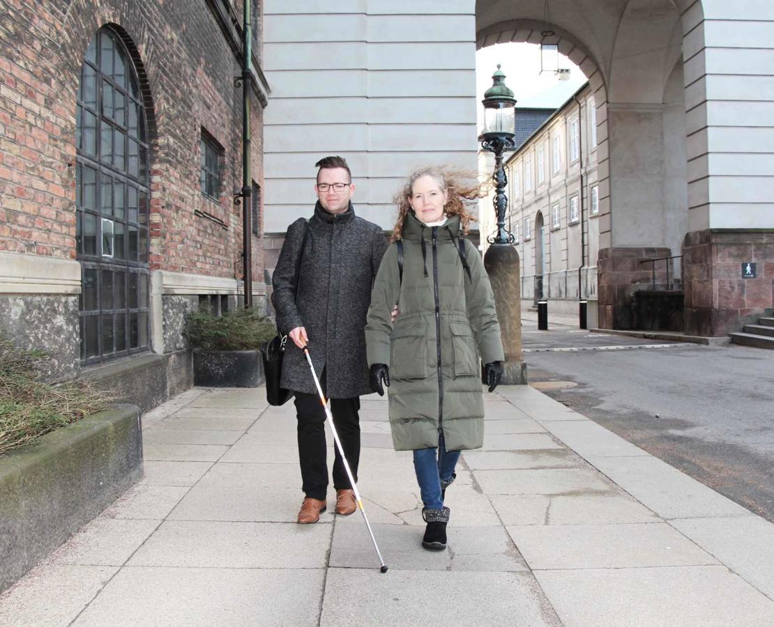 Ung døvblind mand med hvid stok ledsages af sin kontaktperson